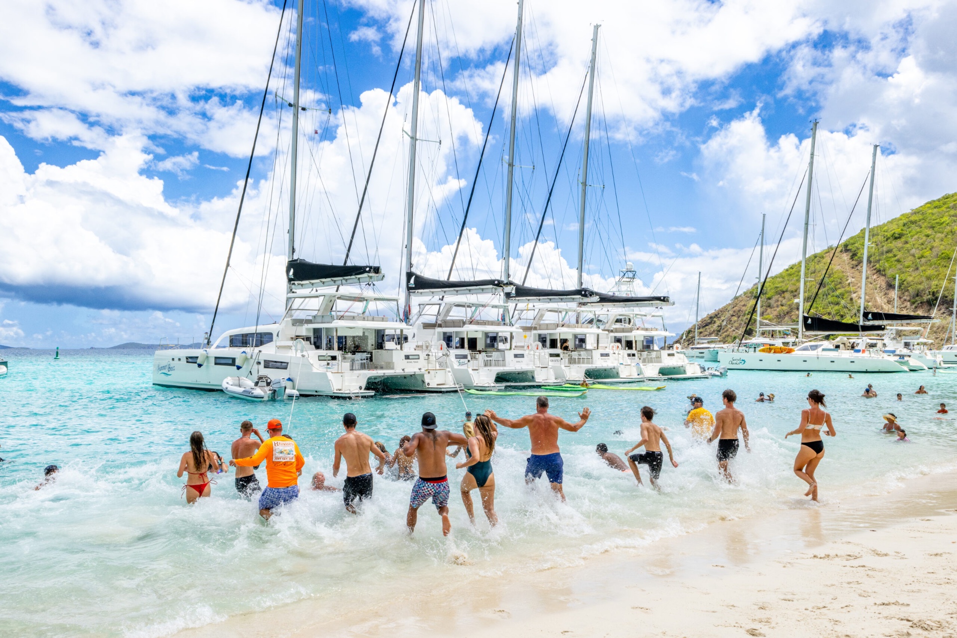 Guests running into shallow water beside anchored Voyage 590 catamarans